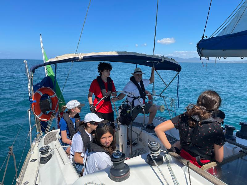 Al campo estivo vela i ragazzi sono in barca nel mare e con il giubbotto di salvataggio seguiti da un istruttore