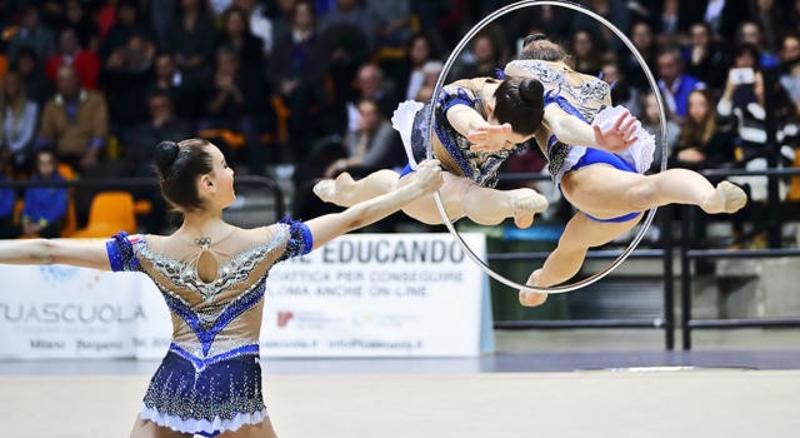Al campo estivo ginnastica ritmica una ragazza regge il cerchio mentre altre due eseguono acrobazie all'interno
