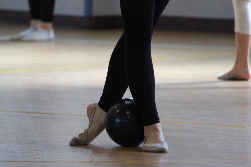 Una ragazza del campo estivo ginnastica ritmica mette la palla nera in mezzo ai piedi