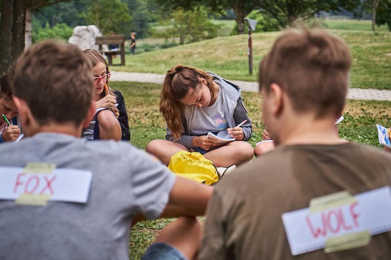 Al campo estivo Emilia Romagna, alcuni ragazzi seduti in cerchio sul prato fanno un gioco per imparare l'inglese