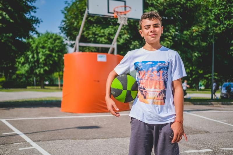Un ragazzo del campo estivo arte regge un pallone da basket verde e dà le spalle al canestro