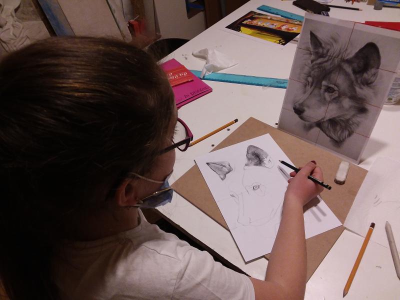 Una bambina disegna un lupo con la matita su un foglio al campo estivo arte