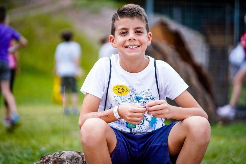 Un ragazzo del campo estivo arte è seduto su un tronco e sorride divertito