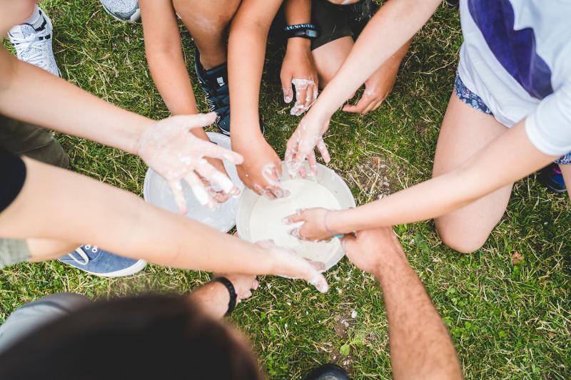 Un gruppo di partecipanti del campo estivo arte immergono le proprie mani in due bacinelle contenenti una sorta di impasto