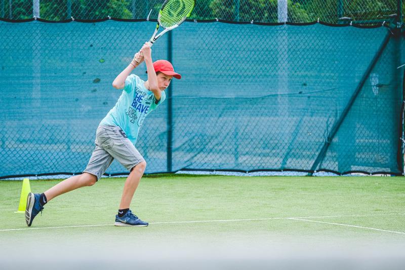 Un ragazzo del campo estivo arte esegue un rovescio a due mani perfetto durante un allenamento di tennis