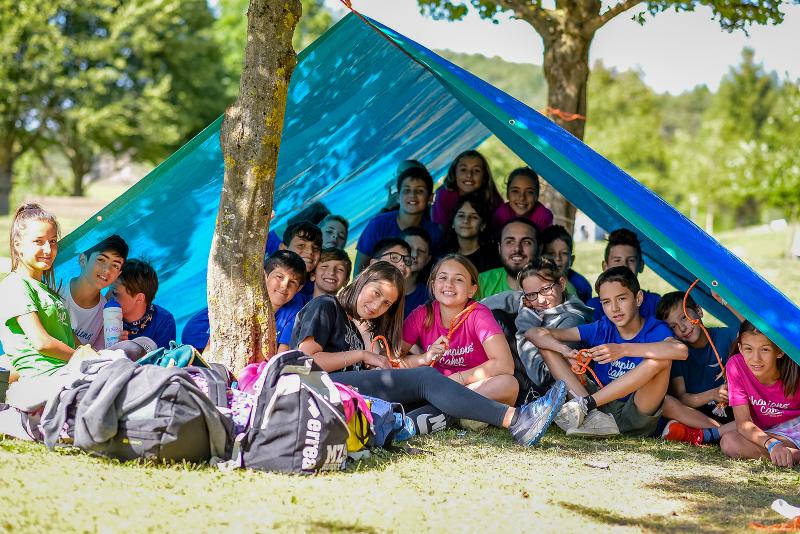 Al campo estivo Trentino Alto Adige i bambini si trovano sotto a una tenda blu con un istruttore
