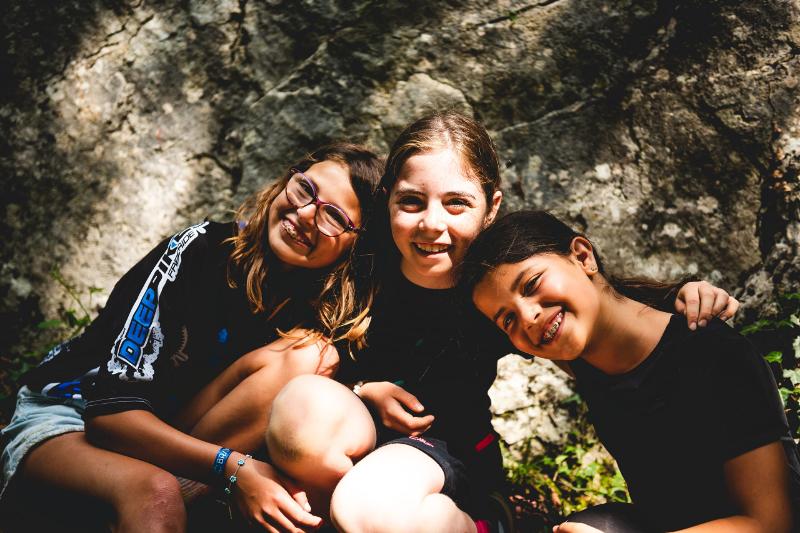 Tre ragazze del campo estivo avventura in montagna stanno sorridendo abbracciate