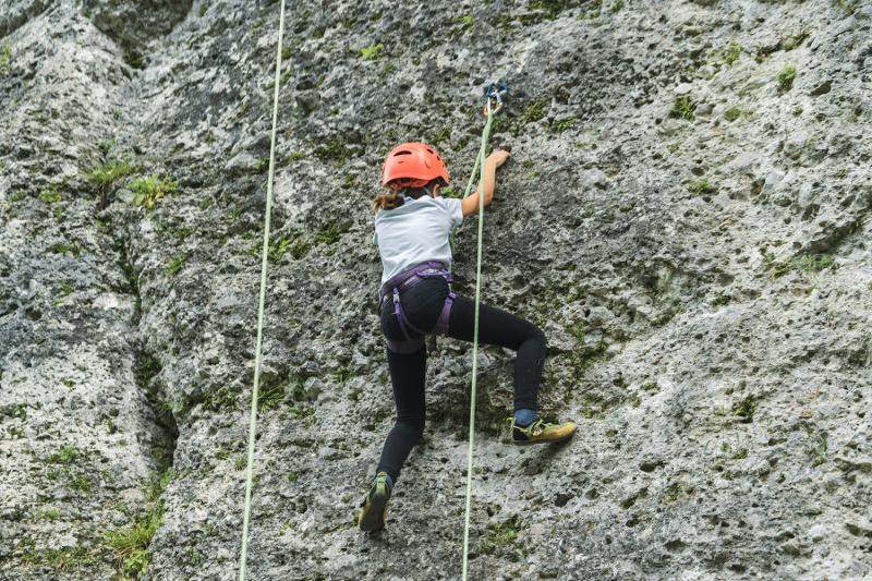 Una bambina del campo estivo avventura si arrampica sulla parete rocciosa di una montagna