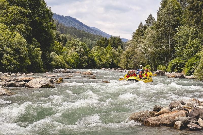 Un gommone di ragazzi ai viaggi organizzati Trento sfreccia tra le rocce e le onde del fiume agitato