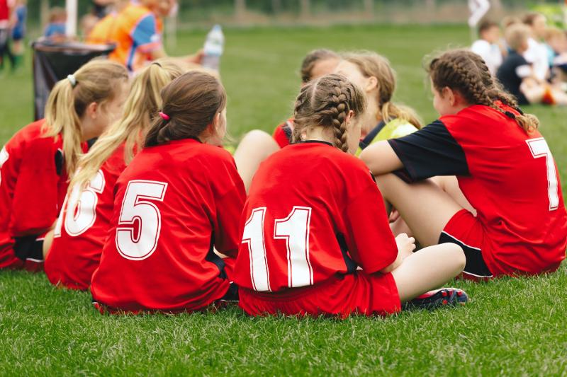 Un gruppo di ragazze del campo estivo calcio è seduto in cerchio in campo