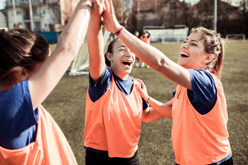 Tre ragazze del campo estivo calcio si danno il cinque ridendo 