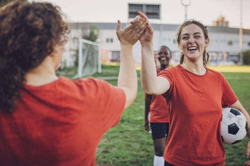 Due ragazze del campo estivo calcio si danno il cinque mentre una regge un pallone in mano 
