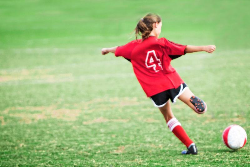 Una ragazza del campo estivo calcio indossa la maglia numero quattro e sta per calciare il pallone in porta