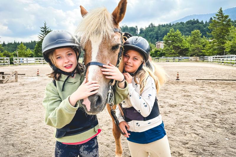 Due bambine abbracciano affettuosamente un cavallo al campo estivo equitazione
