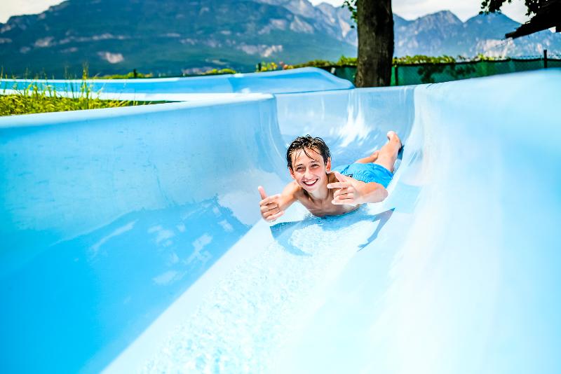 Nel campo estivo equitazione, un ragazzo sorride mentre prova uno scivolo d'acqua azzurro
