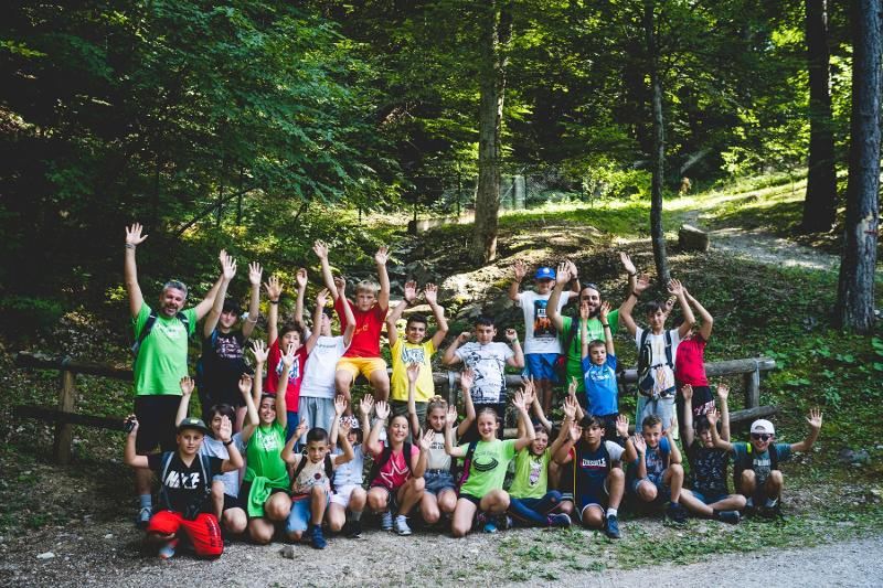 Un grande gruppo di partecipanti e istruttori del campo estivo magia alza le mani al cielo per una fantastica foto di gruppo in montagna
