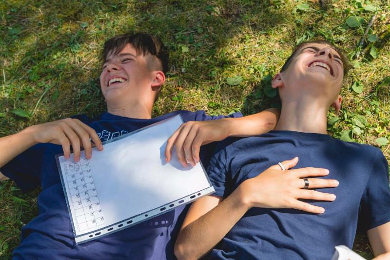 Due ragazzi del campo estivo tecniche di memoria ridono a crepapelle sdraiati in un parco