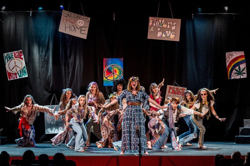 I partecipanti del campo estivo musical eseguono canti e coreografie a tema hippie durante il saggio finale