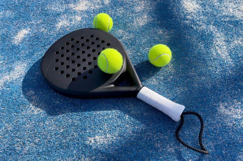 Una racchetta nera del campo estivo Padel è appoggiata sul campo assieme a tre palline