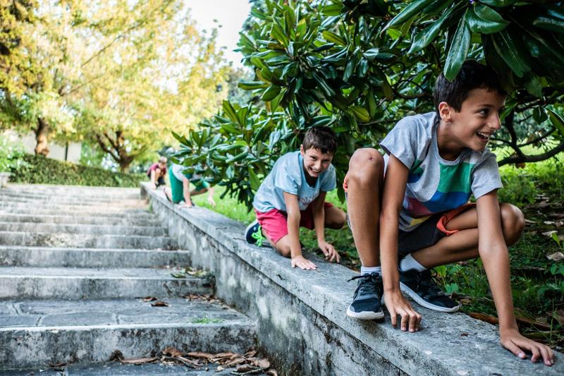 Due bambini partecipanti al campo estivo Parkour saltano agilmente sul muretto di una scala