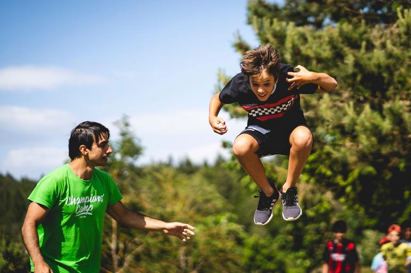 Un ragazzo esegue un salto perfetto al campo estivo Parkour mentre l'istruttore lo assiste