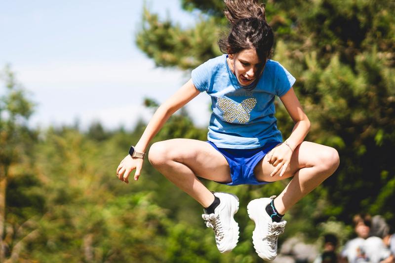 Una ragazza del campo estivo Parkour salta a ginocchia alte