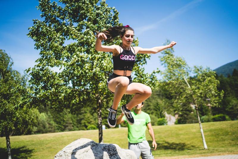 Una ragazza salta da una roccia con l'assistenza di un istruttore del campo estivo Parkour