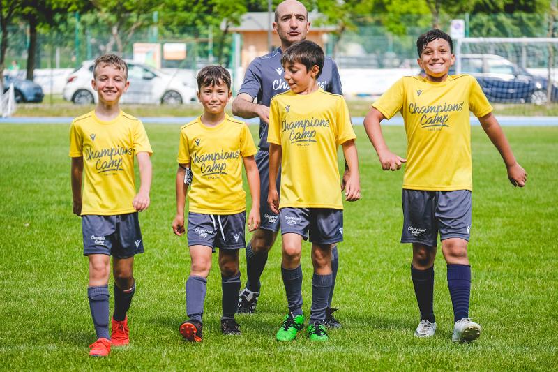 Quattro sorridenti partecipanti del campo estivo calcio camminano in campo seguiti da un coach
