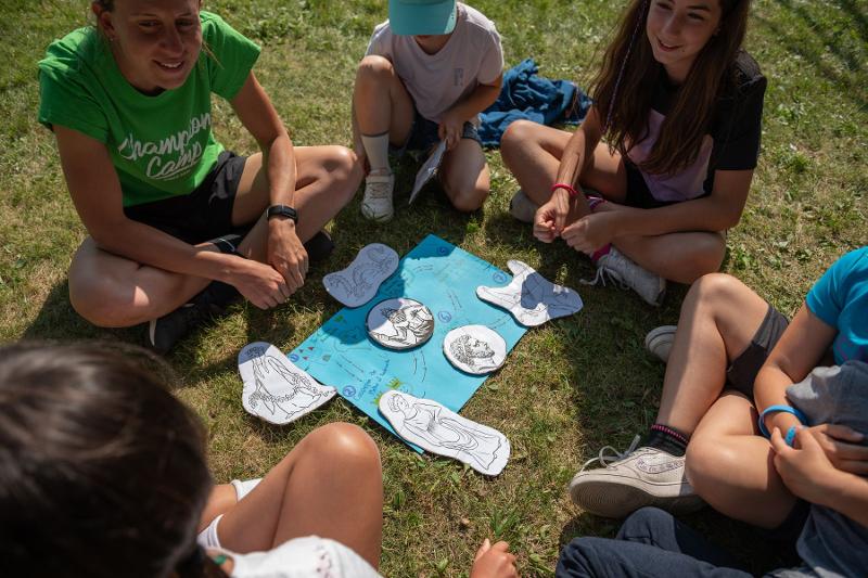 Un gruppo di ragazzi del campo estivo inglese e sport è seduto attorno a un grande foglio e svolge un'attività