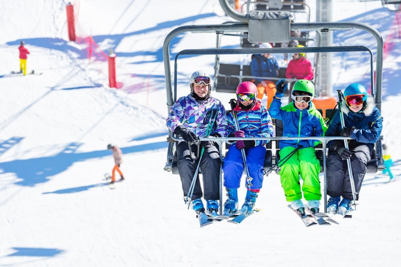 Quattro partecipanti del campo invernale sci e snowboard attendono di risalire la pista sulla seggiovia