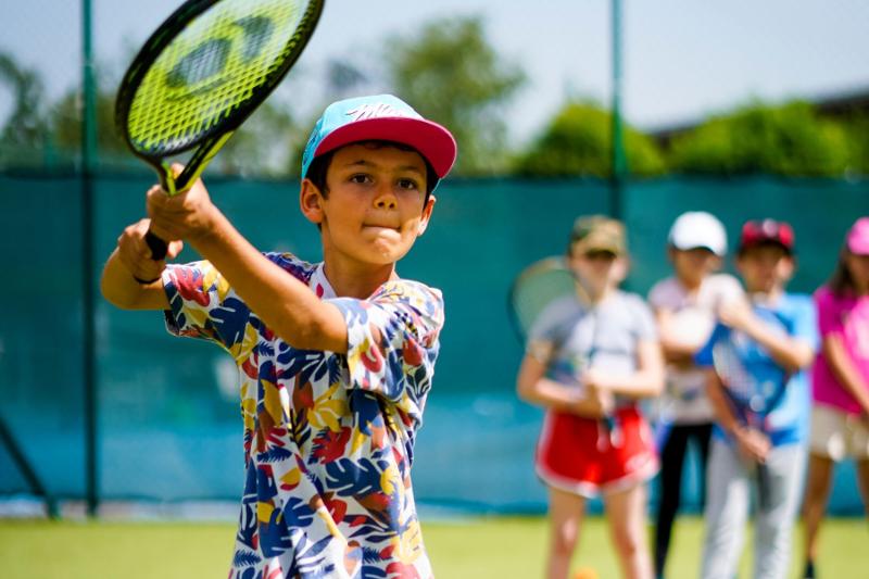 Un partecipante del campo estivo multisport è molto concentrato durante un allenamento di tennis