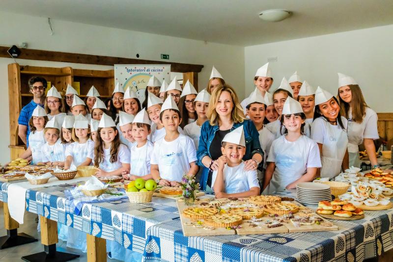 Il gruppo dei partecipanti al campo estivo cucina sono davanti a dei tavoli imbanditi 