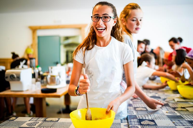 Al campo estivo cucina una ragazza con la coda e con gli occhiali mescola con un mestolo mentre sorride