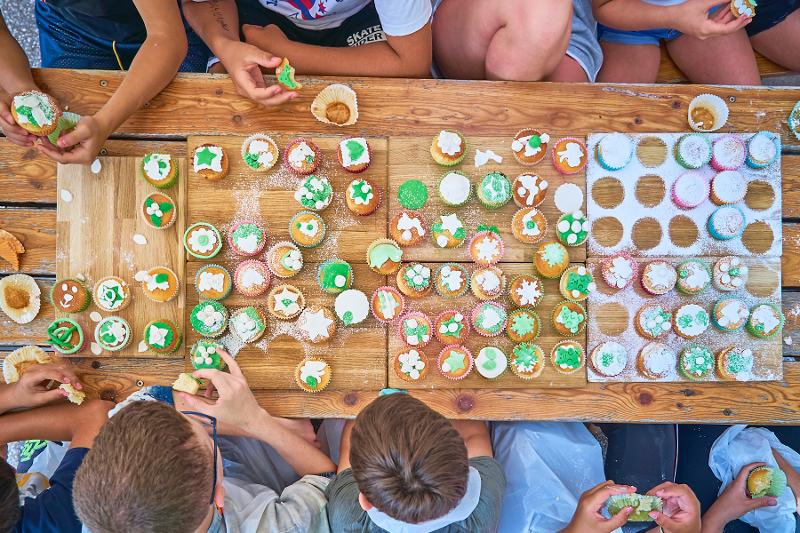 I bambini seduti al tavolo stanno degustando dei dolcetti con dello zucchero verde al campo estivo cucina