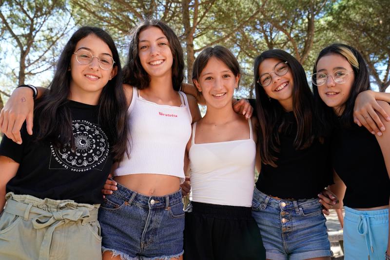 Cinque ragazze si abbracciano mentre viene scattata loro una foto all'aria aperta al campo estivo inglese Roma