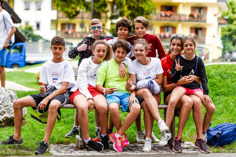 Un gruppo di amici del campo estivo di inglese in montagna è seduto su una panchina per una foto di gruppo 