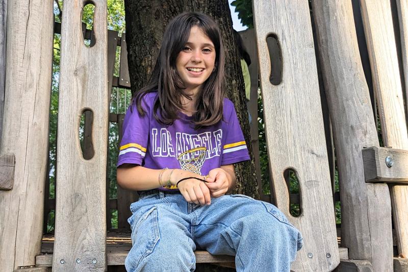 Una giovane partecipante del campo estivo di inglese è seduta su una struttura in legno e indossa una maglietta viola