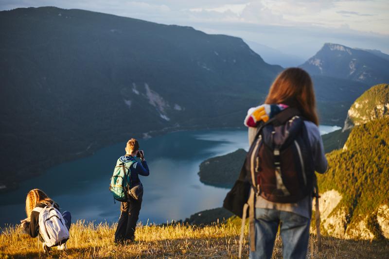 Al campo estivo Trentino Alto Adige tre ragazzi cercano la posizione ottimale per scattare in cima a un rilievo con sotto un lago