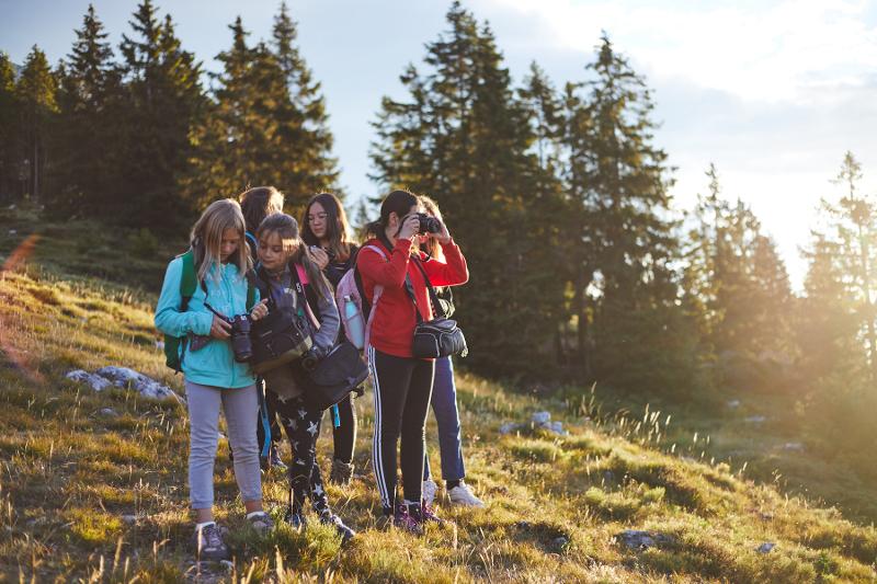 Al campo estivo fotografia un gruppo di ragazze scatta e guarda foto al tramonto sul prato