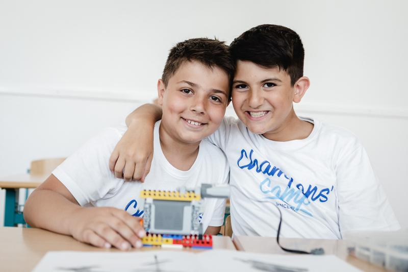 Due bambini sorridono e hanno davanti una piccola costruzione colorata al campo estivo Trentino Alto Adige di Lego