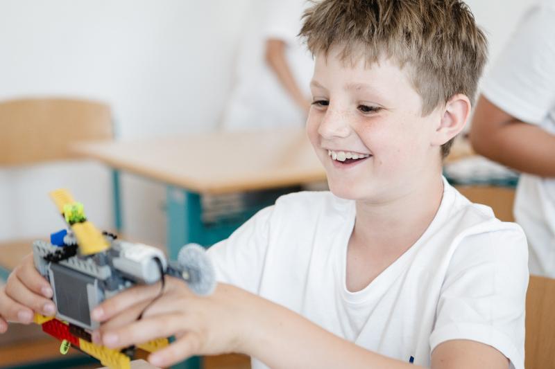 Un bambino biondo sorride mentre impugna un oggetto che ha costruito al campo estivo Trentino Alto Adige di Lego