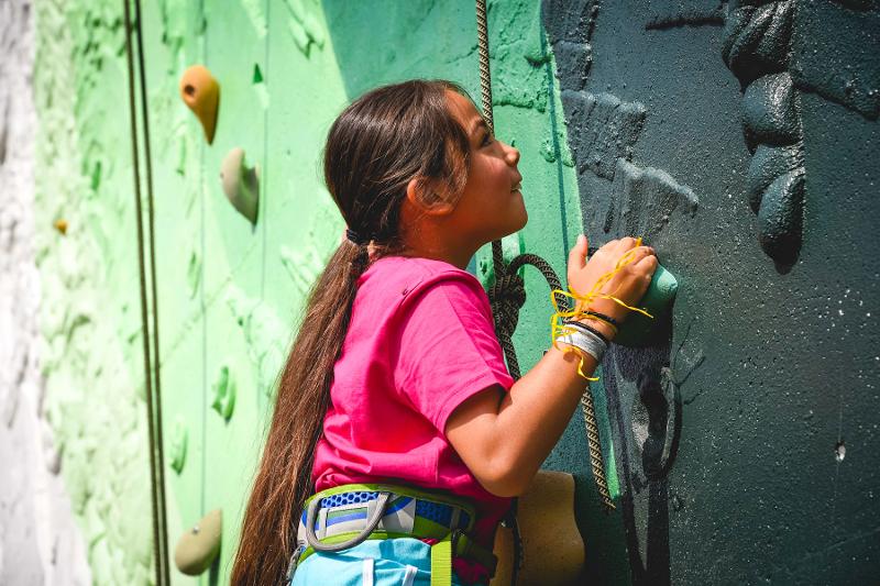 Una bambina prova l'arrampicata su muro con le imbracature al campo estivo multisport