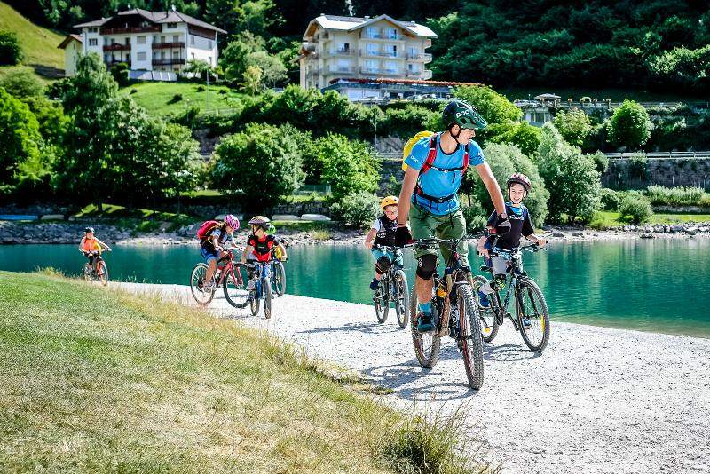Al campo estivo attività, alcuni bambini stanno facendo un giro in bici lungo un fiume con il supervisore