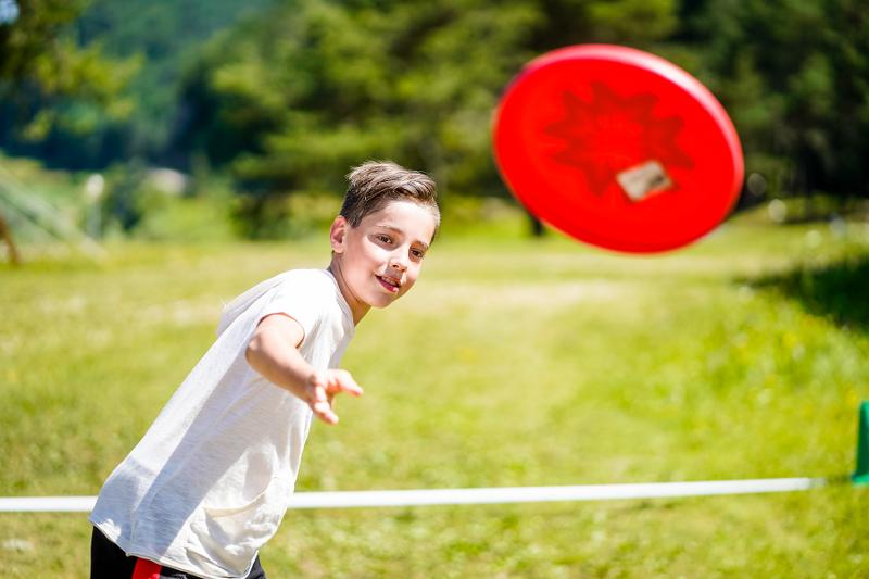 Al campo estivo multisport un ragazzo lancia un frisbee rosso nel prato 