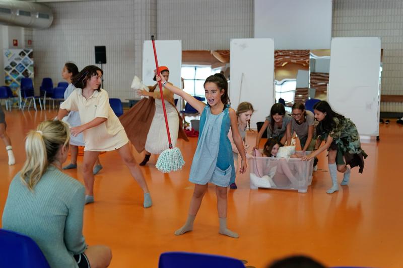 Una bambina impugna una scopa e altri intorno a lei sono travestiti e mettono in scena un balletto al campo estivo recitazione