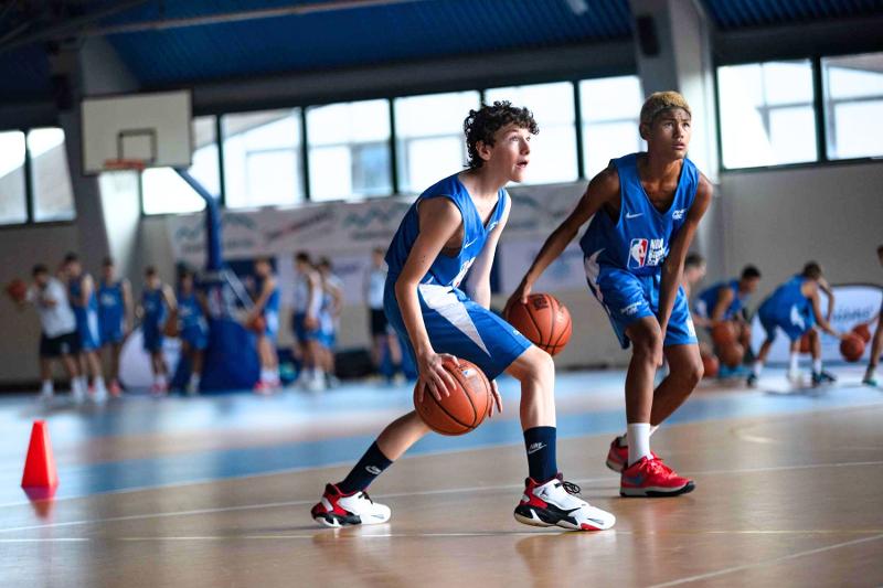 Due ragazzi del campo estivo basket palleggiano sincronizzati guardando il canestro