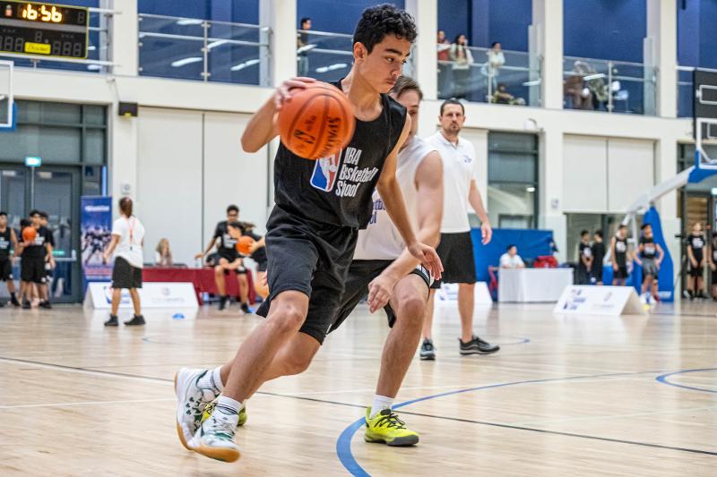 Un ragazzo con la divisa nera palleggia cercando di aggirare l'avversario al campo estivo basket