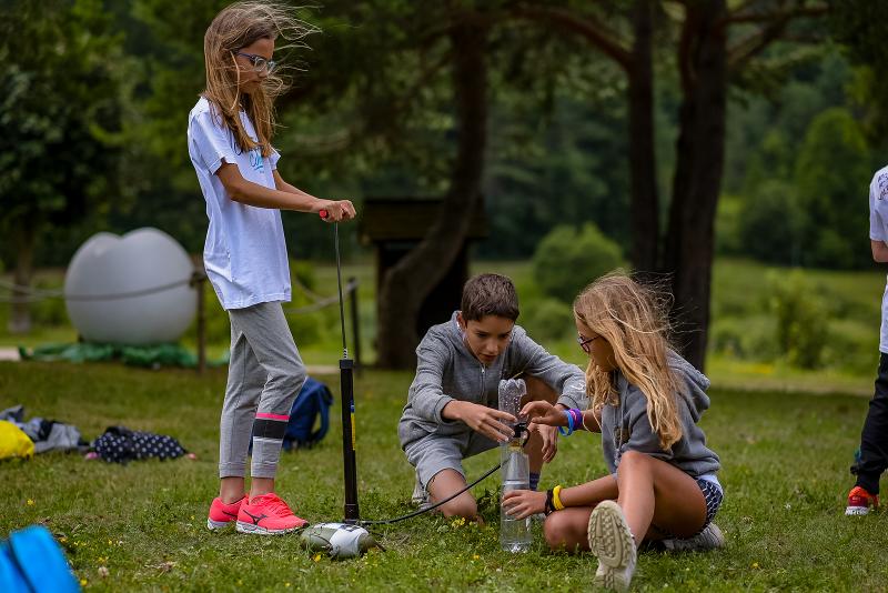 Avvicinati al verde e prova nuove esperienze ai campi estivi natura Durante i campi estivi naturalistici, tre bambini provano a costruire un macchinario con delle bottiglie di plastica su un prato