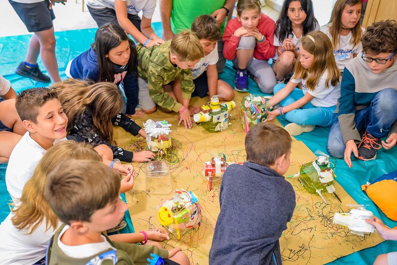 Condividerai l'amore e il rispetto per la natura nei campi estivi natura Ai campi estivi naturalistici, tanti bambini sono attorno a un tappeto dove stanno progettando giochi con materiali riciclabili