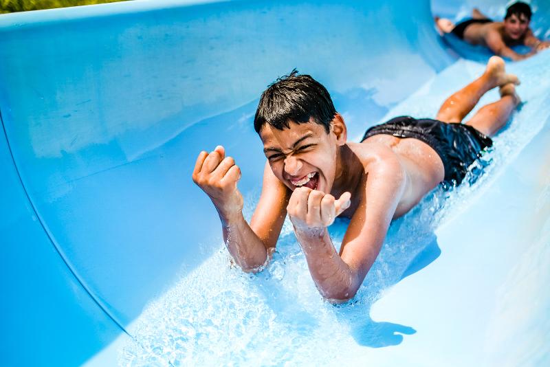 Al campo estivo Puglia, un ragazzino sorride scendendo giù da uno scivolo d'acqua azzurro